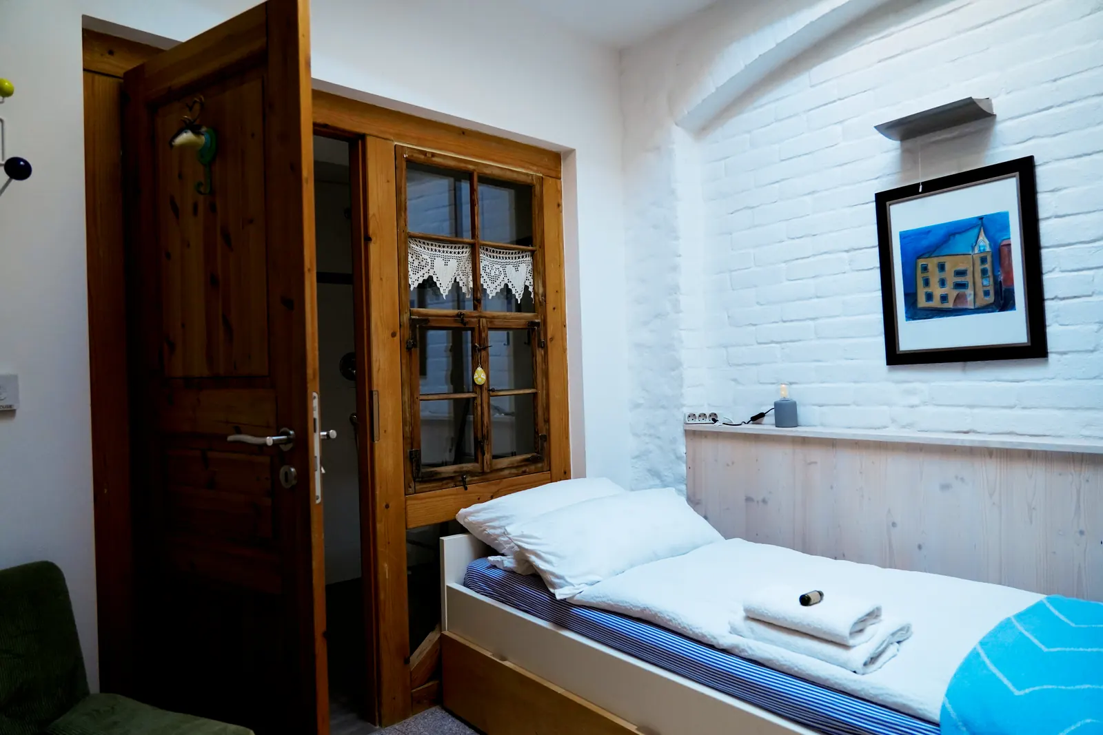 Einzelzimmer mit weiß getünchter Backsteinwand, Bett und Blick ins eigene Bad